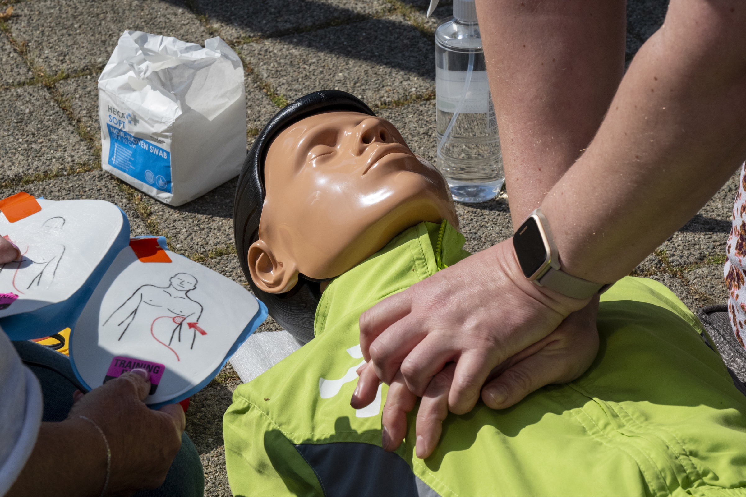 Cursist oefent reanimatie op een pop met een AED-trainer ernaast